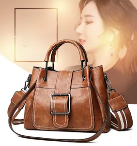 Brown bucket bag with white contrast stitching and a stylish striped shoulder strap