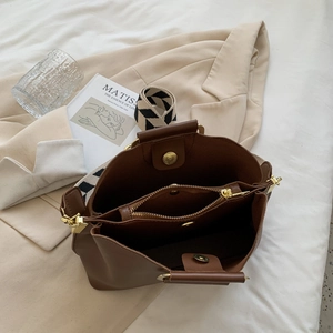 Brown leather bucket bag with geometric strap and three-compartment interior layout