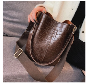 Detail of dark brown crocodile embossed bucket bag with wide strap and gold hardware
