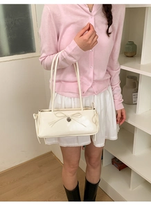 Detail of a creamy white bow shoulder bag with heart pendant and long elegant handles