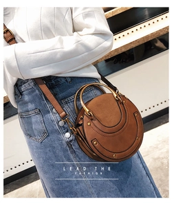 Detail of round brown crossbody bag with gold metal handle and matte leather stitching
