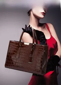 Detail of a dark brown crocodile pattern tote bag with polished finish and gold metal accents