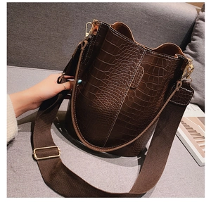 Detail of dark brown crocodile-embossed bucket bag with wide fabric strap and gold hardware