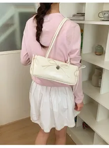 Close-up of cream white glossy underarm bag with bow decor and heart pendant on shoulder