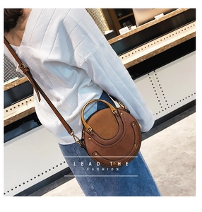 Detail shot of a brown round crossbody bag with metal U-handle and adjustable strap