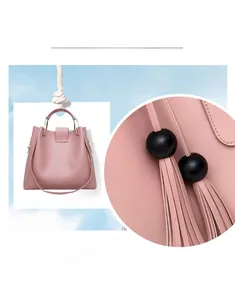 Detail of pink faux leather handbag with metal handle, long fringe and black ball charm