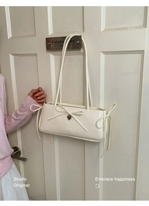Detail of cream shoulder bag with bow tie and engraved metal heart pendant charm