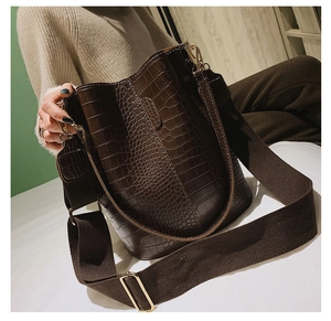 Detail of dark brown crocodile embossed bucket bag with wide woven strap and gold hardware