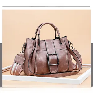 Close-up of brown textured leather bucket bag with metal buckle and woven strap