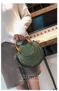 Dettaglio della borsa rotonda verde scuro con manico in metallo dorato e borchie