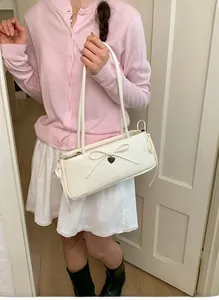Close-up of a white shoulder bag with a delicate bow and metal heart charm on a pink sweater