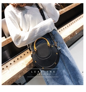 Detail of a black round crossbody bag with matte leather and a gold semicircular handle