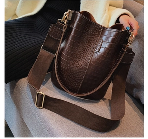 Close-up of dark brown crocodile pattern bucket bag with wide strap and gold hardware
