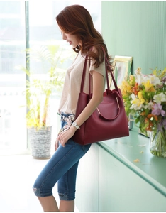 Deep red large capacity tote bag with gold ring handle and long strap shown with model