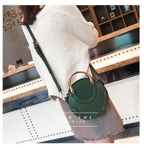 Dettaglio della borsa rotonda verde scuro con manico dorato e tracolla in un ambiente da caffè