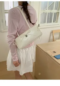 Detail of white patent leather shoulder bag with bow and heart charm on a model