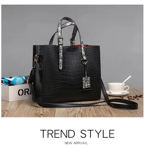 Detail of black crocodile texture tote bag with snake print handles and red lining