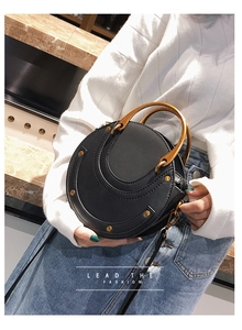 Detail of round black leather bag with gold semi-circle metal handle and rivet accents