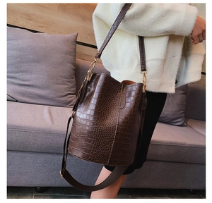 Close-up of brown crocodile texture bucket bag with gold metal hooks and adjustable strap