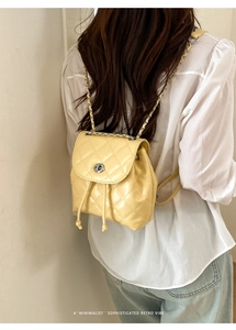 Detail of yellow quilted mini backpack featuring chain straps and metallic turn-lock
