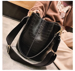 Detail of black crocodile texture bucket bag with wide canvas strap and gold buckle