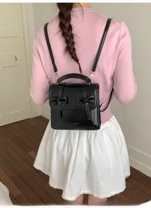 Detalle de mochila negra brillante con adornos de lazos dobles y cierre de solapa