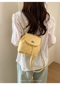 Detail view of yellow quilted mini backpack with leather-interwoven chain straps on model