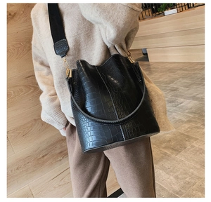Detail of black crocodile pattern bucket bag featuring gold hardware and wide strap
