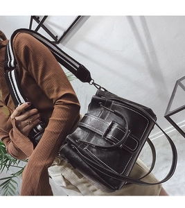 Close-up of black bucket bag with white contrast stitching and striped web strap