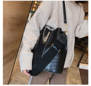 Detail of black crocodile texture bucket bag with wide strap and gold-tone hardware