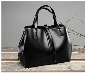 Detail of a black leather tote bag featuring a metal buckle and a smooth polished finish