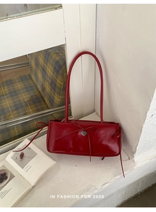 Close-up of deep red leather shoulder bag with a bow tie and silver heart pendant
