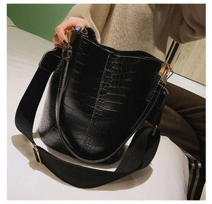 Detail of black crocodile texture bucket bag with wide fabric strap and gold hardware