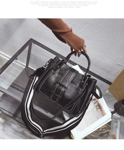 Detail of black leather bucket bag with metal buckle and striped wide shoulder strap