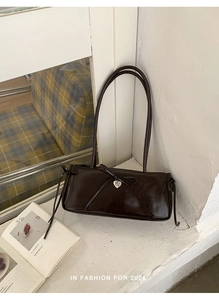 Close-up of brown glossy shoulder bag featuring ribbon bow and silver heart pendant detail