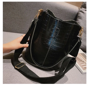 Detail of black crocodile texture bucket bag with wide canvas strap and gold hardware