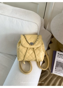 Detail of yellow quilted backpack with diamond stitching and metal chain on white sofa