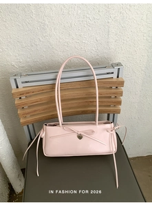 Detail of light pink shoulder bag with bow and heart pendant on a wooden chair