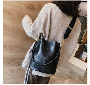 Detail of crocodile pattern texture on black bucket bag with wide fabric shoulder strap