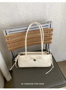 Close-up of cream bow shoulder bag featuring a heart pendant and fine stitching detail