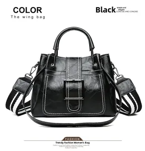 Detail view of black wing bucket bag with white contrast stitching and striped strap
