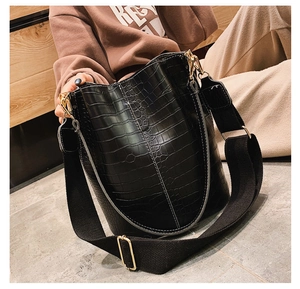 Detail of black crocodile texture bucket bag with wide fabric strap and golden hardware
