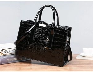 Detail of black crocodile texture tote bag with metallic hardware on a wooden desk