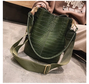 Detail of dark green crocodile pattern bucket bag with wide olive textile shoulder strap