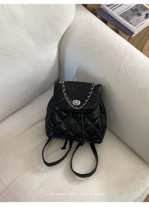 Detail of black quilted mini backpack with silver twist lock and metal chain on sofa