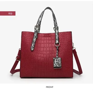 Detail of red faux leather tote bag with crocodile pattern and snakeskin print handles