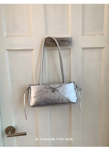 Detail of silver rectangle underarm bag with leather bow and heart metal charm