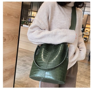 Detail of dark green crocodile texture bucket bag with wide canvas shoulder strap