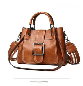 Detailed side view of brown bucket bag with white contrast stitching and striped strap