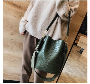 Detail of dark green crocodile texture bucket bag with woven strap and gold hardware